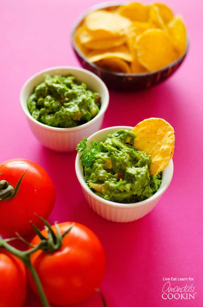 An overhead picture of two white bowls filled with guacamole and two tomatoes sitting on the side.