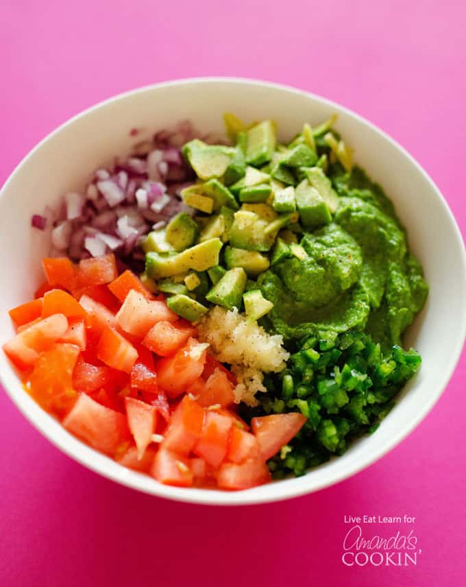 An overhead picture of a white bowl filled with chopped tomatoes, red onion, avocado and jalapeno. 