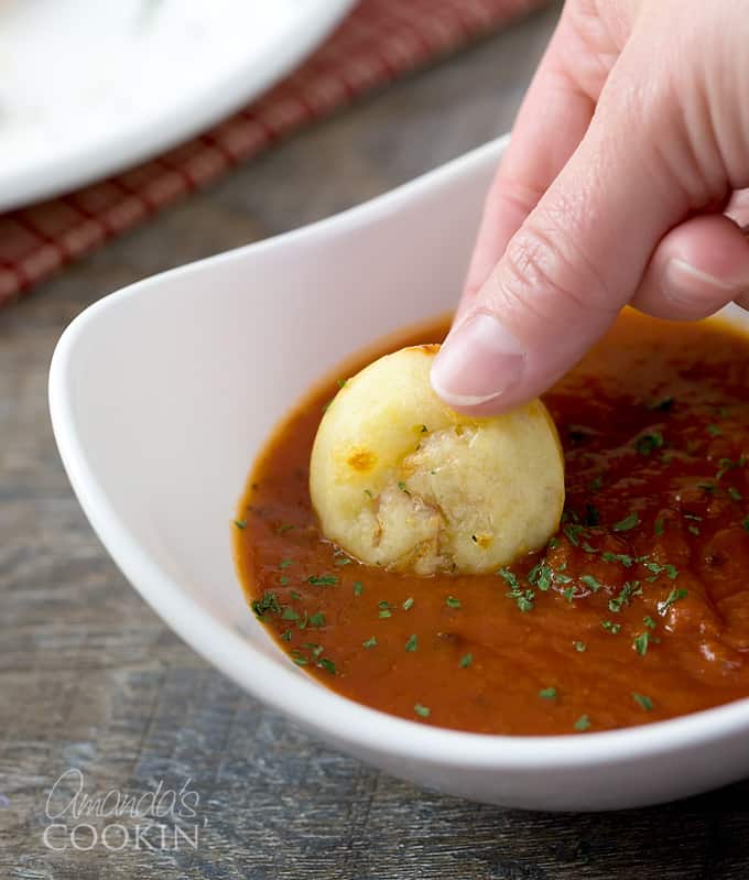 A pizza puff being dunked in a white bowl of pizza sauce.