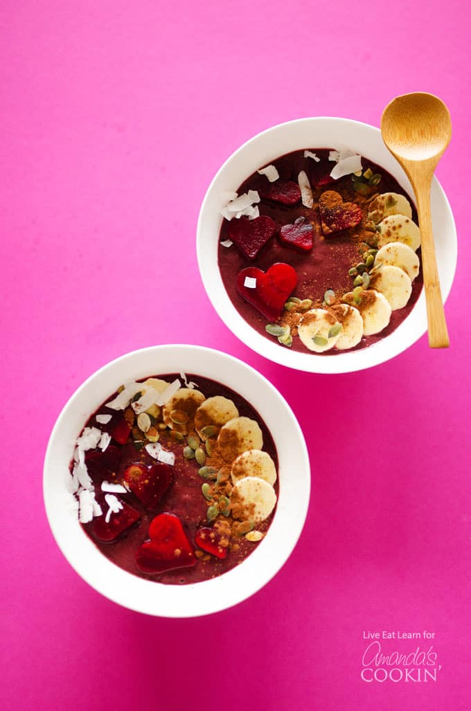 Two white bowls filled with red velvet smoothie and a wooden spoon.