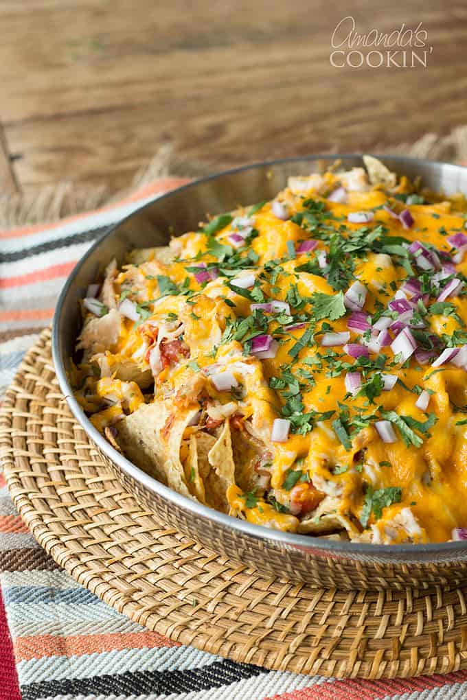 A stainless steel bowl of rotisserie chicken nachos resting on a wicker place mat.