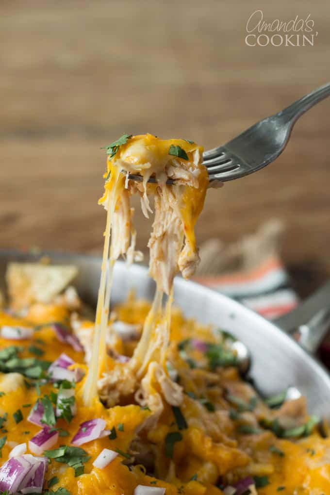 A photo of a fork pulling a piece of cheesy rotisserie chicken nachos from a pan.
