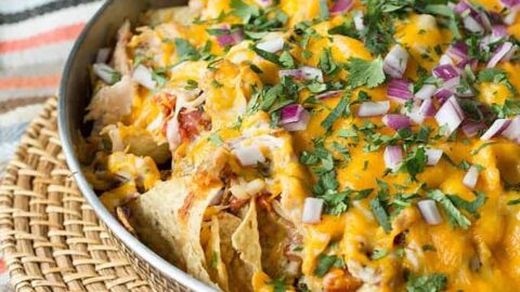 A bowl of loaded rotisserie chicken nachos resting on a wicker place mat.