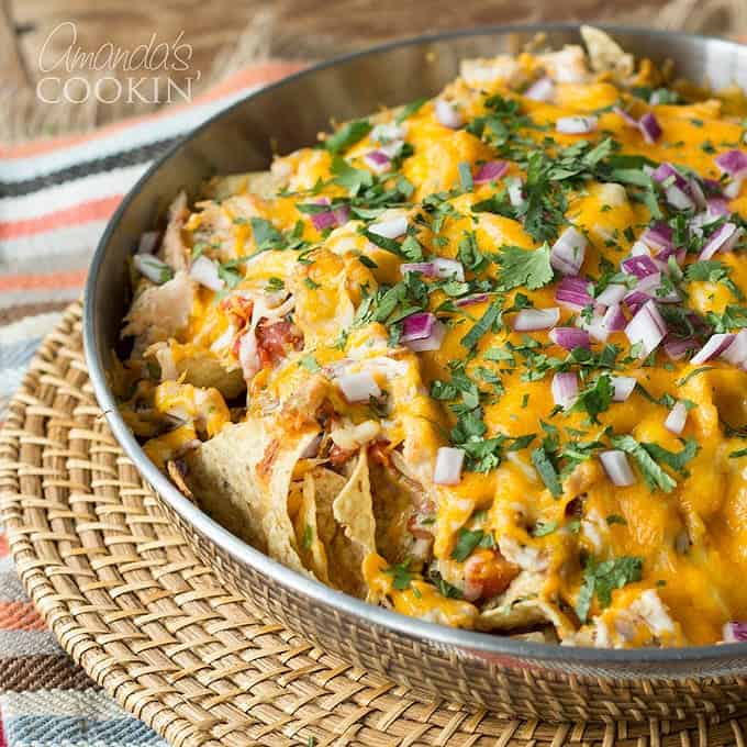 A stainless steel bowl of rotisserie chicken nachos resting on a wicker place mat.