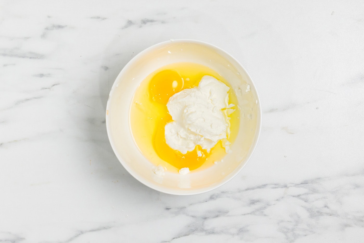 Eggs and ricotta cheese in a white mixing bowl before whisking