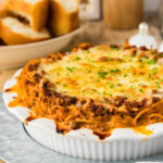 Baked spaghetti pie in a white deep dish pie plate on a galvanized tray with garlic bread