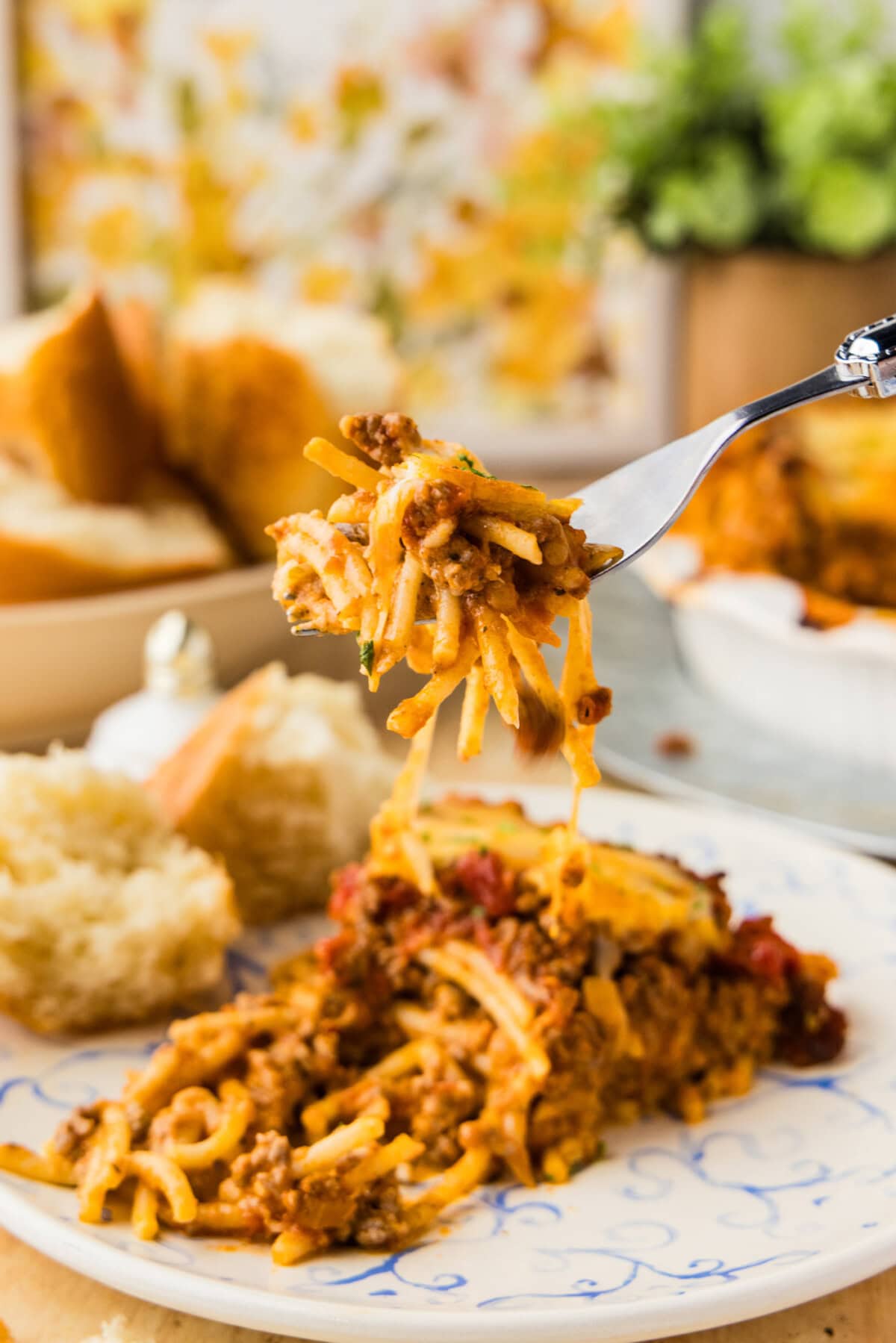 Forkful of spaghetti pie lifted from a slice showing melted cheese and meat sauce