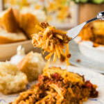 Forkful of spaghetti pie lifted from a slice showing melted cheese and meat sauce