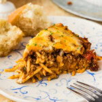 Slice of spaghetti pie on a blue patterned plate with a fork and torn garlic bread