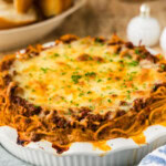 Baked spaghetti pie in a white fluted deep dish pie plate with bread alongside