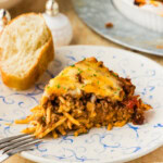 Wedge of spaghetti pie served on a blue and white plate with the full pie behind