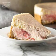 A slice of strawberry swirl cheesecake resting on a white plate.