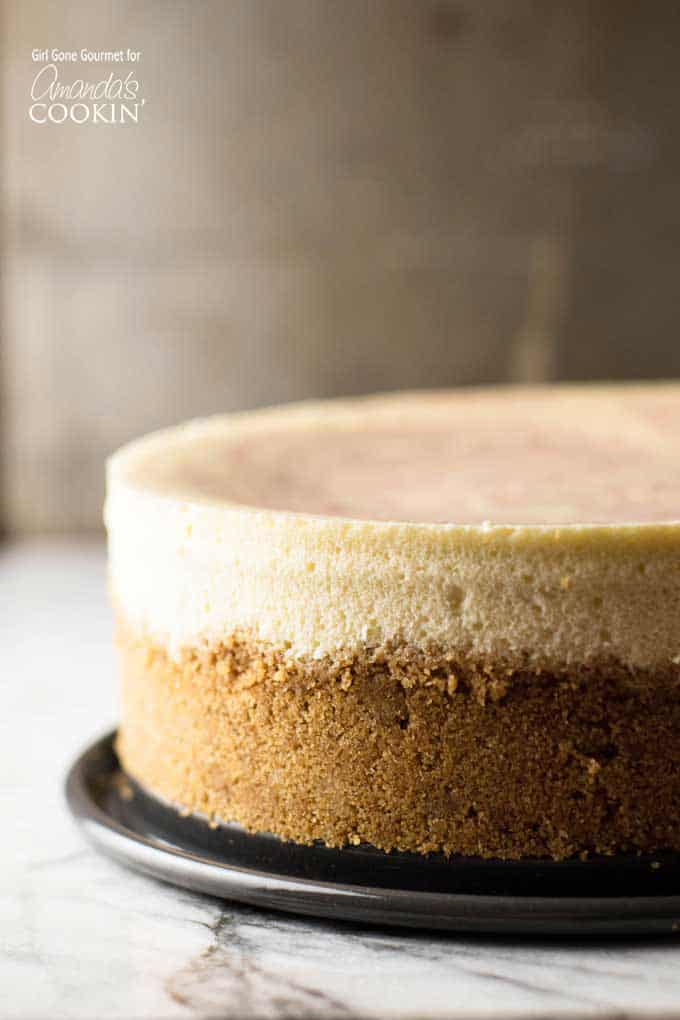 A close up side shot of an entire strawberry swirl cheesecake sitting on a black plate.