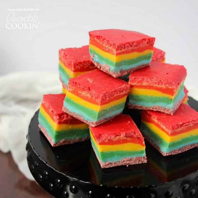 Rainbow fudge squares stacked on a black cake stand.