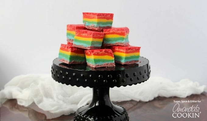Rainbow fudge cubes stacked on a black cake stand.