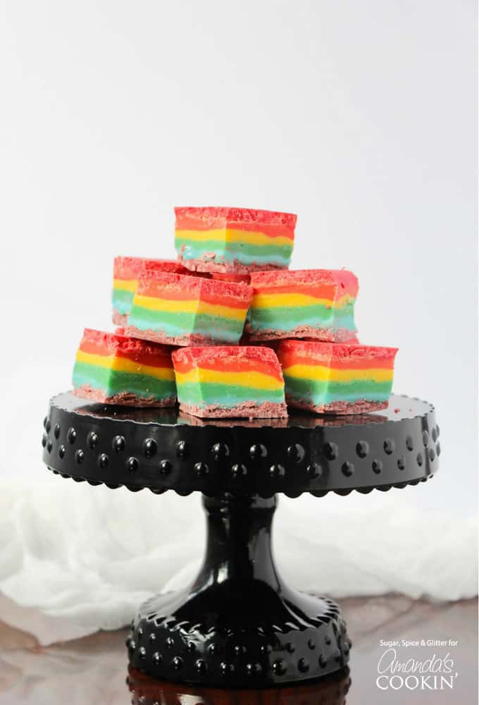 Cubes of rainbow fudge stacked up on a black cake stand.