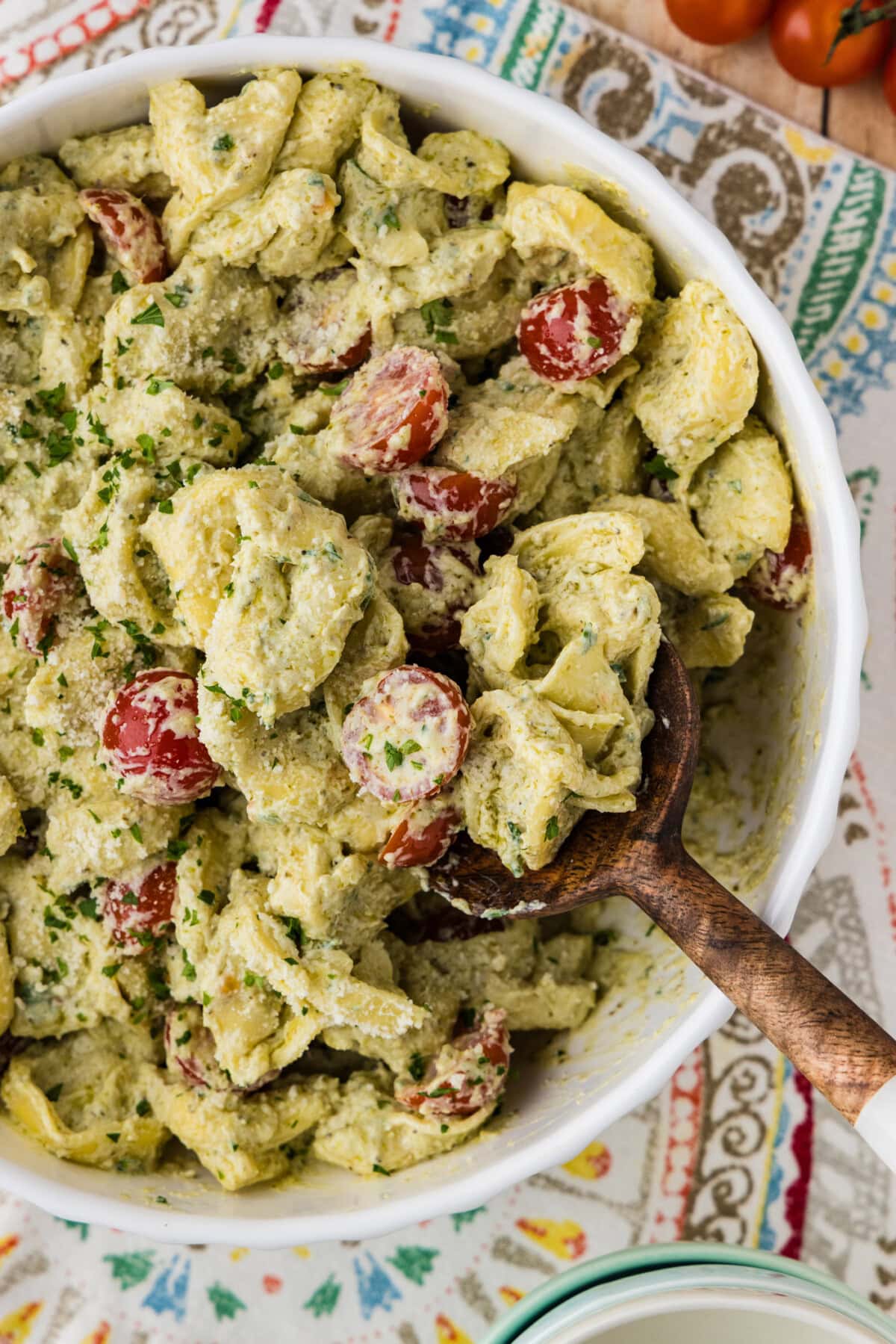 Tortellini Pesto Pasta Salad in serving bowl with wooden spoon