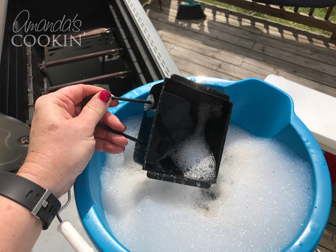 dropping grease catcher from grill into soapy water to soak