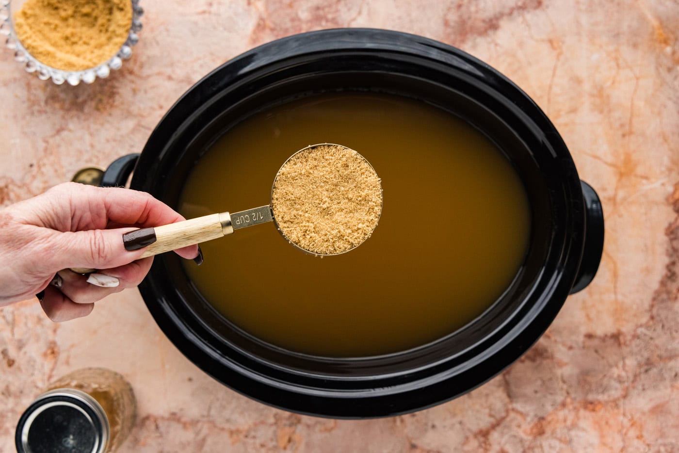 holding brown sugar in a measuring cup over a crockpot