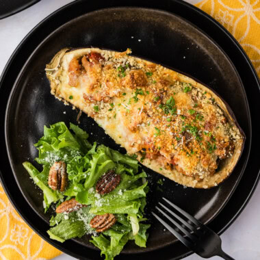 Stuffed Baked Eggplant Parmesan on a black plate with salad