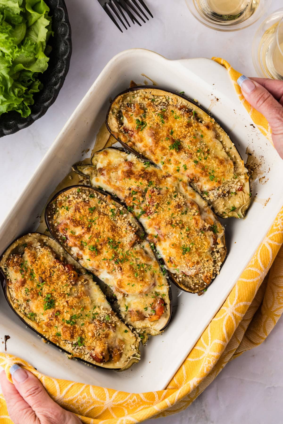 hands lifting a baking dish of stuffed baked eggplant parmesan