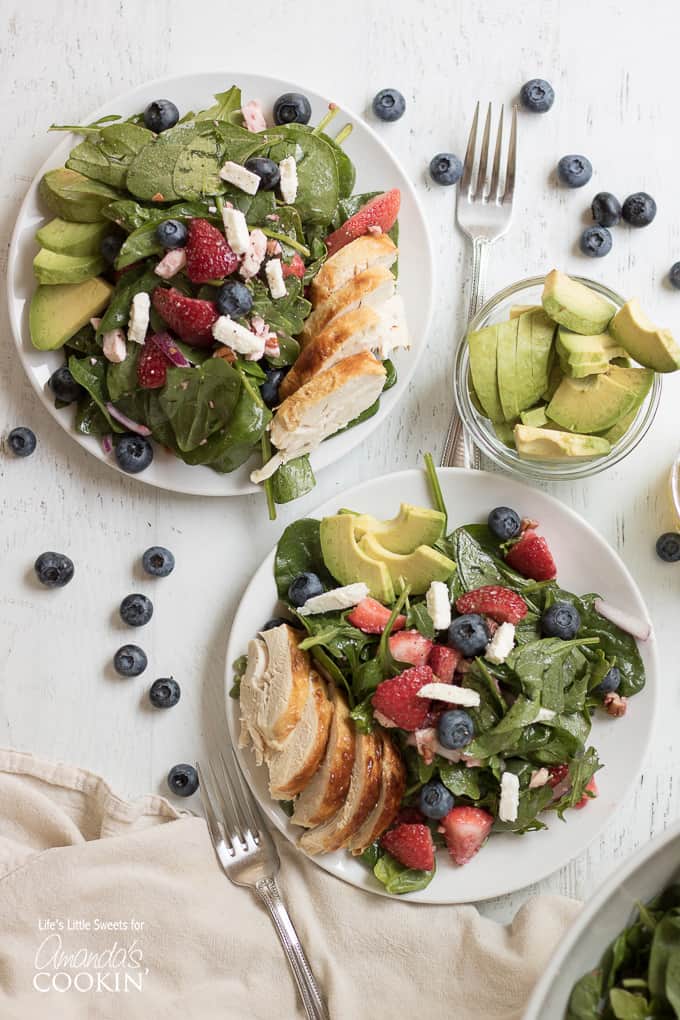 An overhead of two pomegranate clementine spinach salads with scattered blueberries on the table.