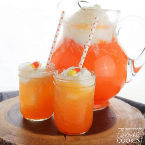 two glasses of candy corn punch with pitcher in background