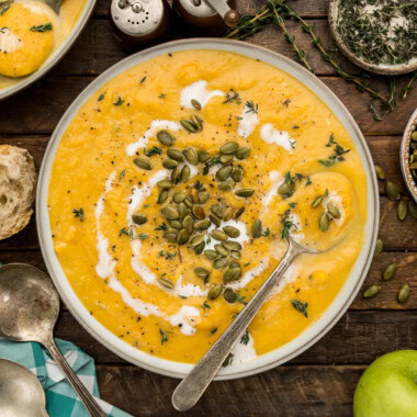 Bowl of creamy butternut squash soup topped with toasted pepitas, coconut milk and fresh thyme with a spoon