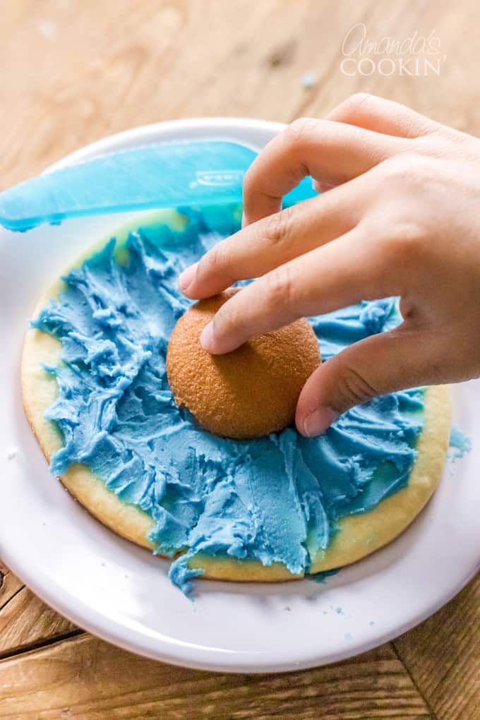 hand placing nilla wafer on frosted cookie