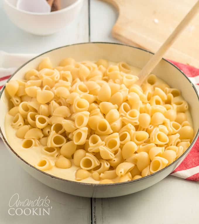 stirring cheese sauce into bowl of pasta
