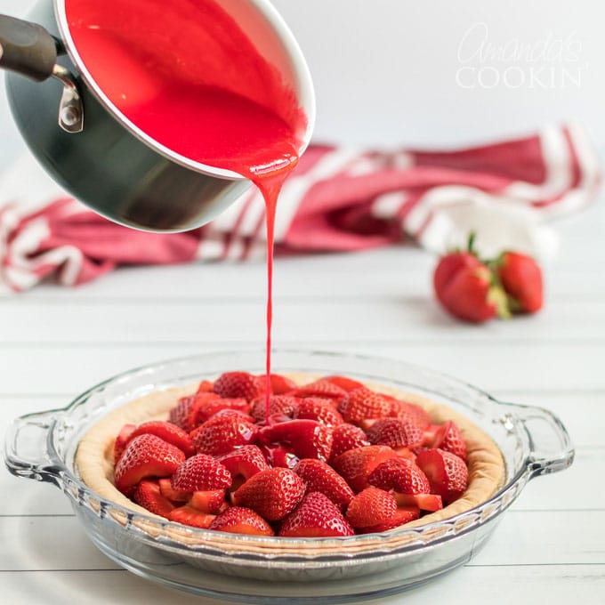 pouring gelatin mixture over strawberries in a pie plate