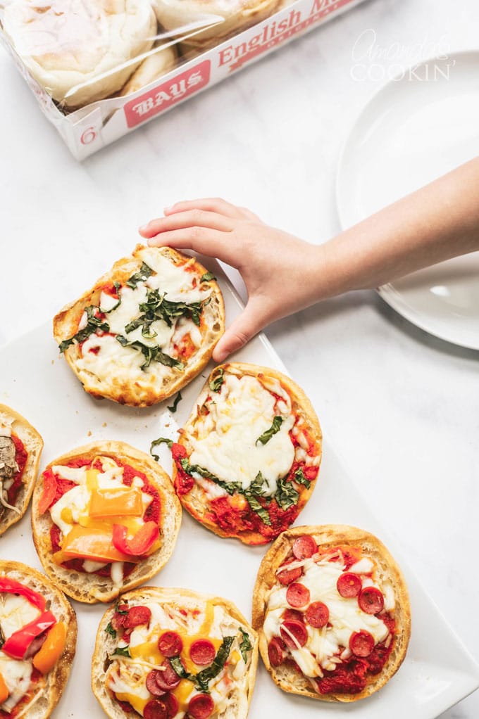 child's hand reaching for an english muffin pizza