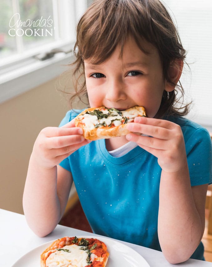 little girl taking bite from english muffin pizza