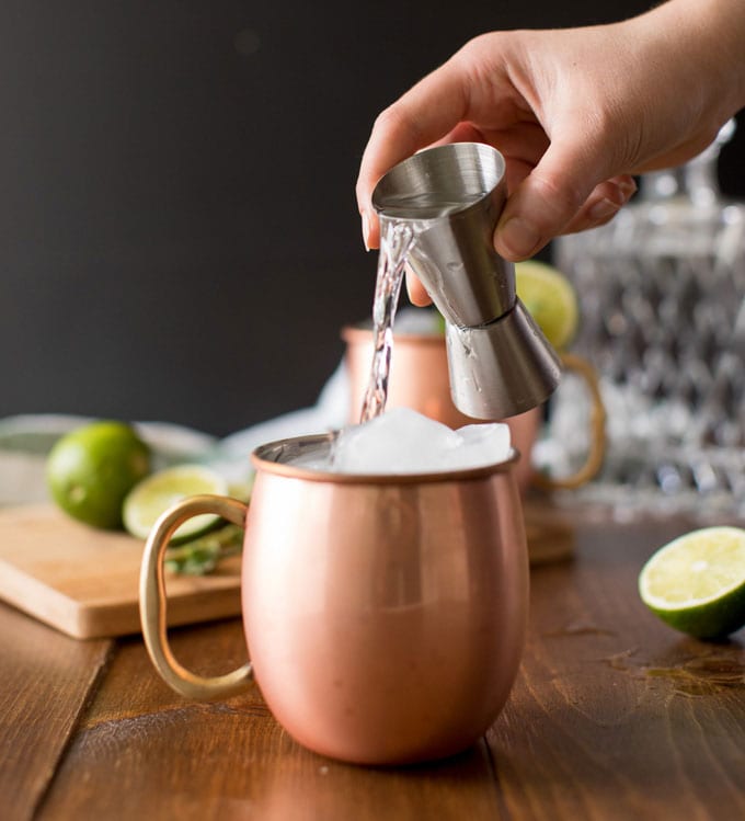 pouring vodka over ice in copper mug