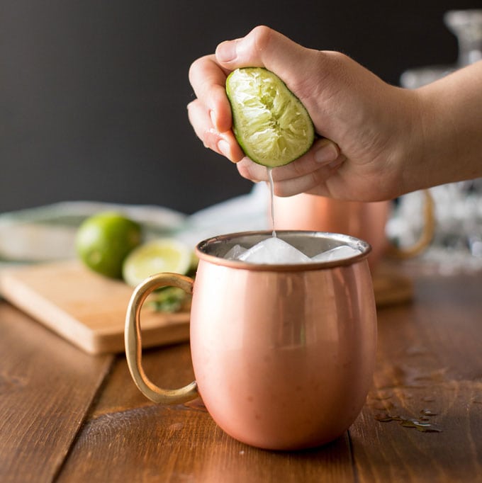 squeezing fresh lime juice into copper mug