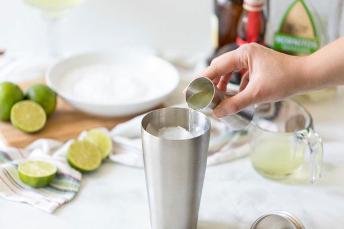 adding tequila to a cocktail shaker to make a margarita