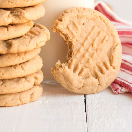 peanut butter cookie with a bite out of it with a stack of cookies and glass of milk
