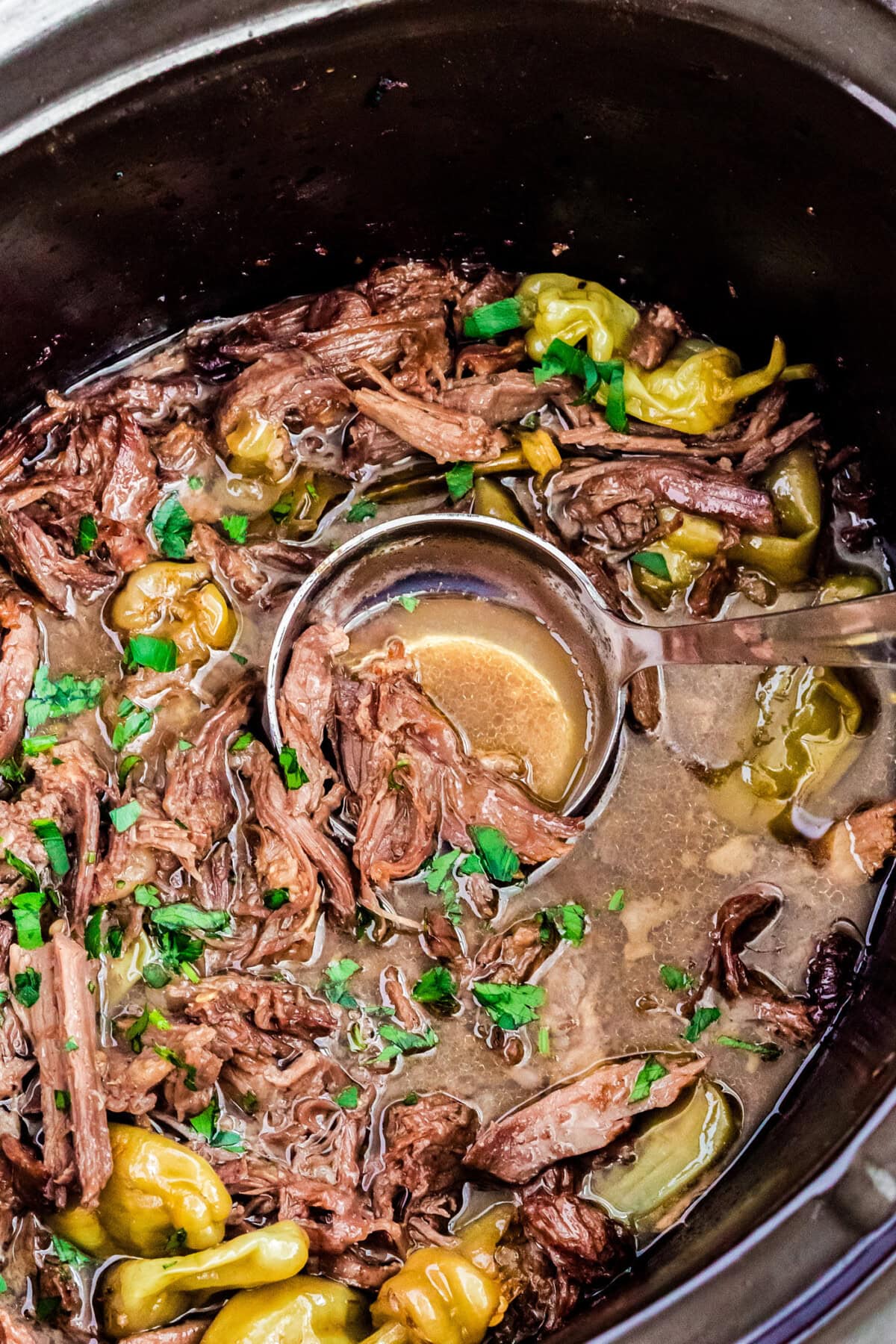 Tender shredded beef with peppers and herbs in slow cooker for Mississippi Pot Roast.