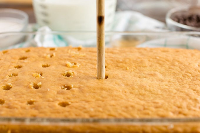 poking holes in a cake with a wooden spoon