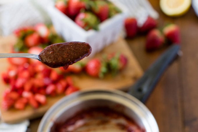 spoon of homemade strawberry jam hovering over saucepan