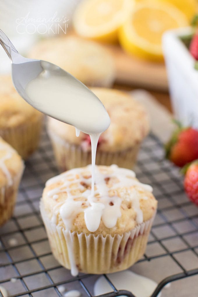 Spoon drizzling glaze over a strawberry muffin on a cooling rack
