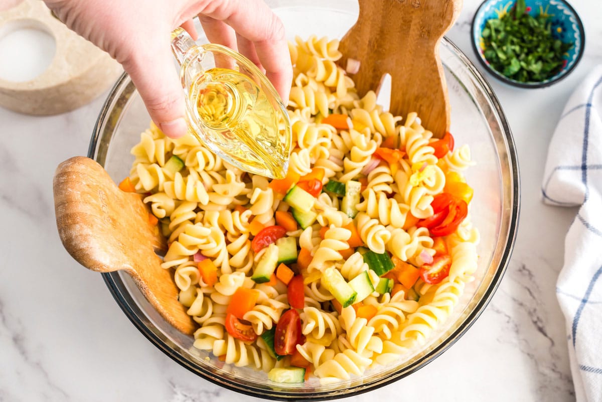 adding olive oil to pasta in a bowl