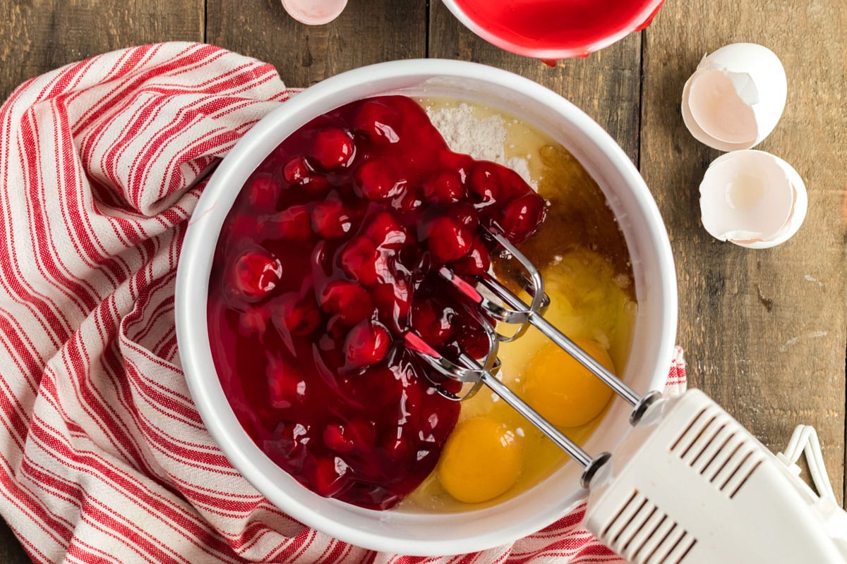 cherry pie filling, eggs, cake mix, in a bowl with a mixer