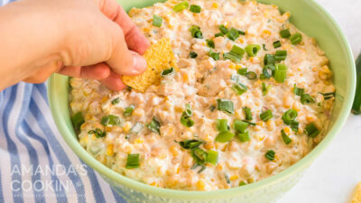 hand dipping tortilla chip in corn dip