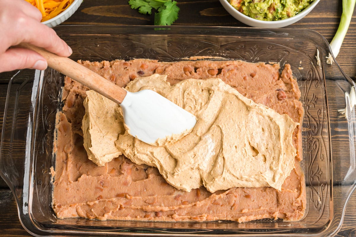 spreading taco seasoning cream cheese mixture over refried beans