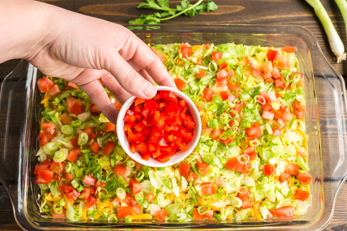 sprinkling toppings over taco dip