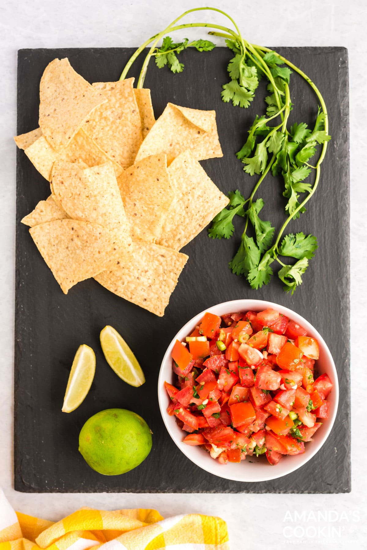bowl of salsa fresca on a black board with chips, cilantro, and limes