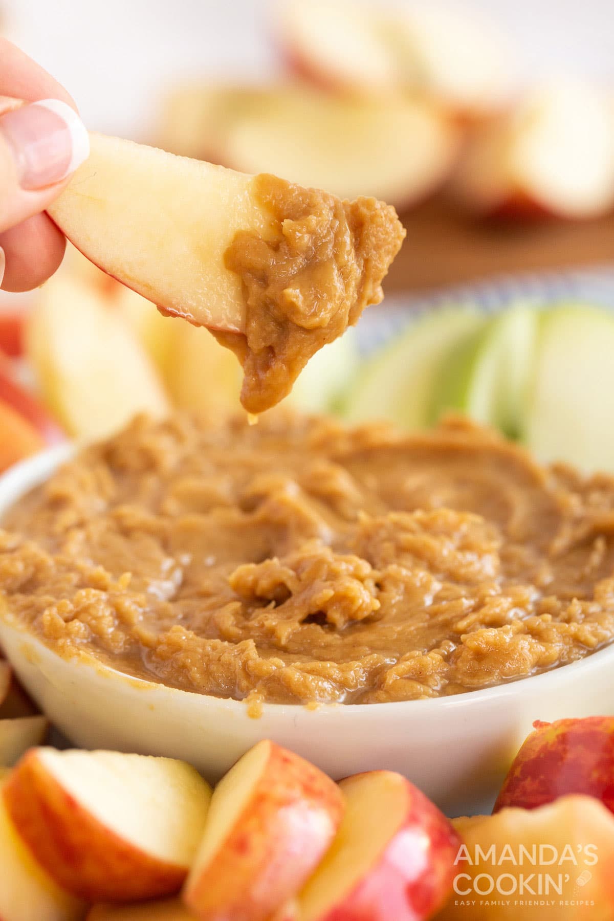 someone holding an apple slice covered with peanut butter dip