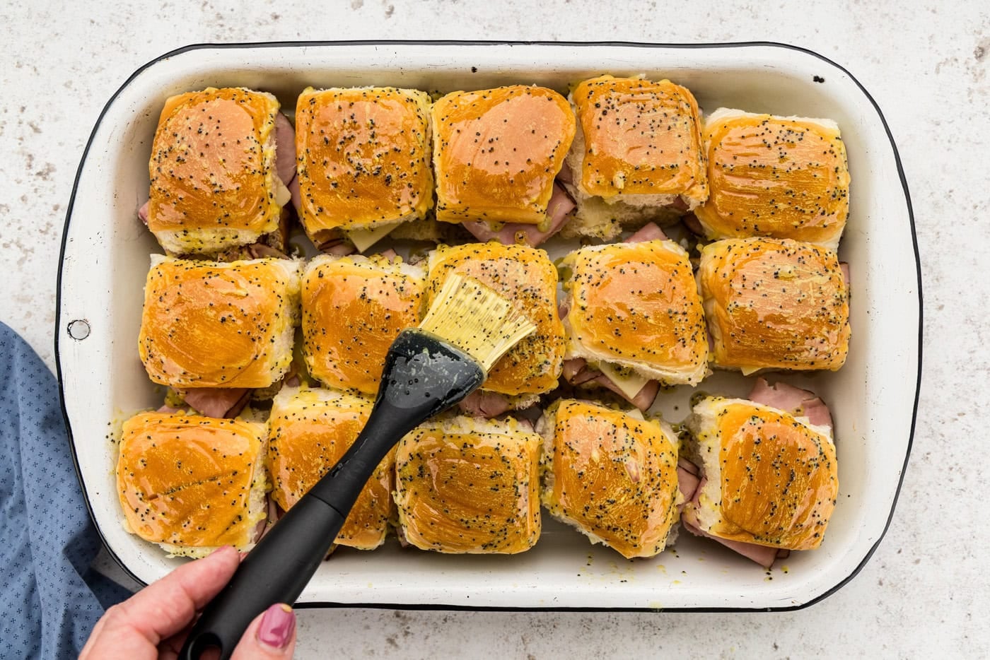 brushing on poppyseed butter topping over ham and cheese sliders