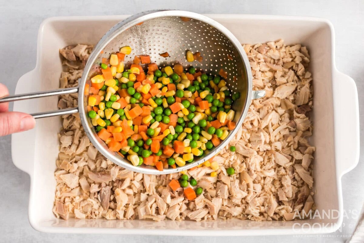 pouring frozen veggies over chicken in a pan